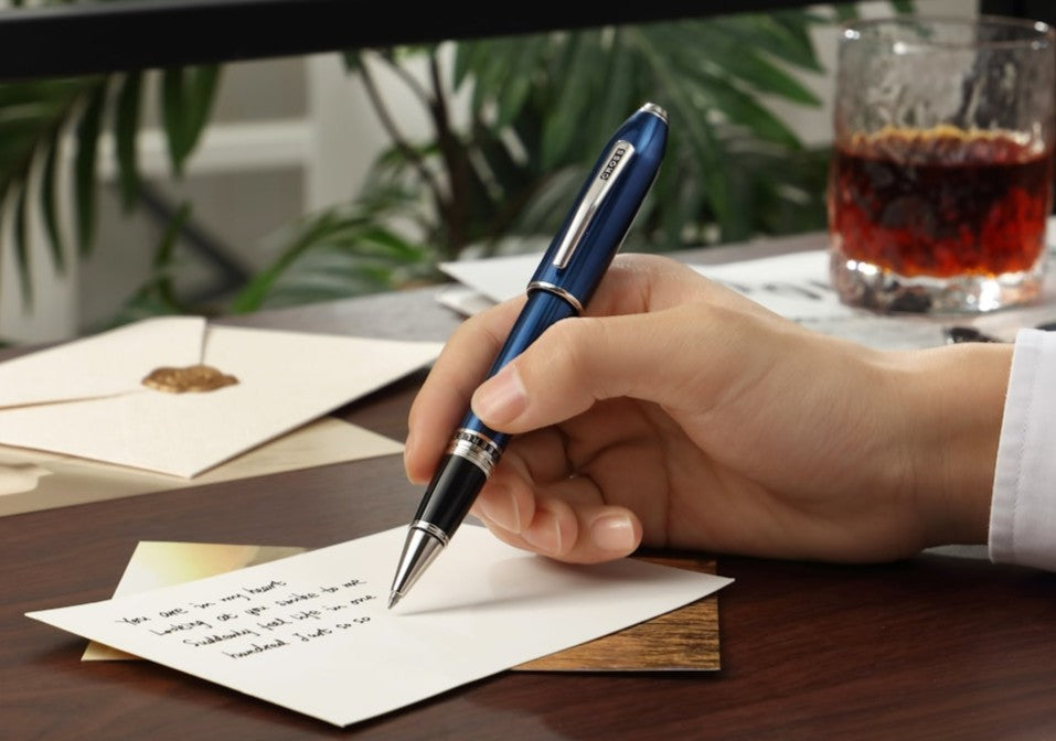 Hand writing on a piece of paper with a blue pen, sitting at a desk.
