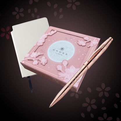 Rose gold pen and pink packaging with floral design on a dark background