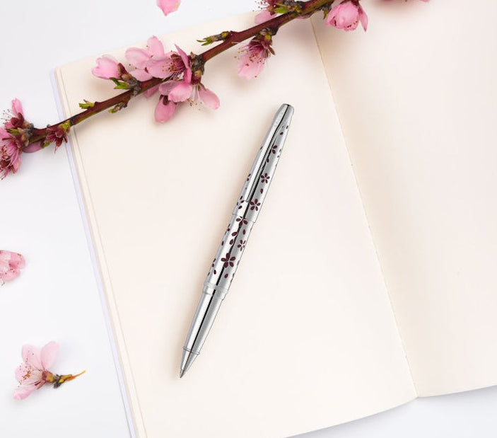 Open notebook with a pen and pink cherry blossom branch on a white background