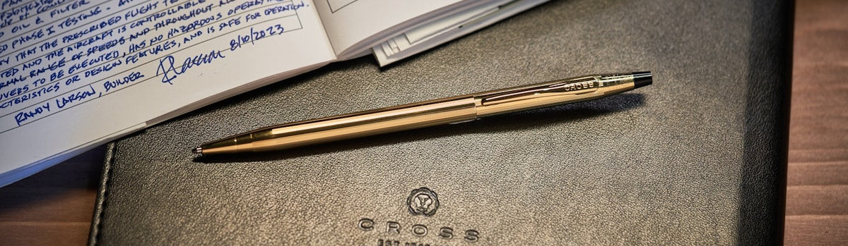 Gold pen on a leather-bound book with text and a logo.